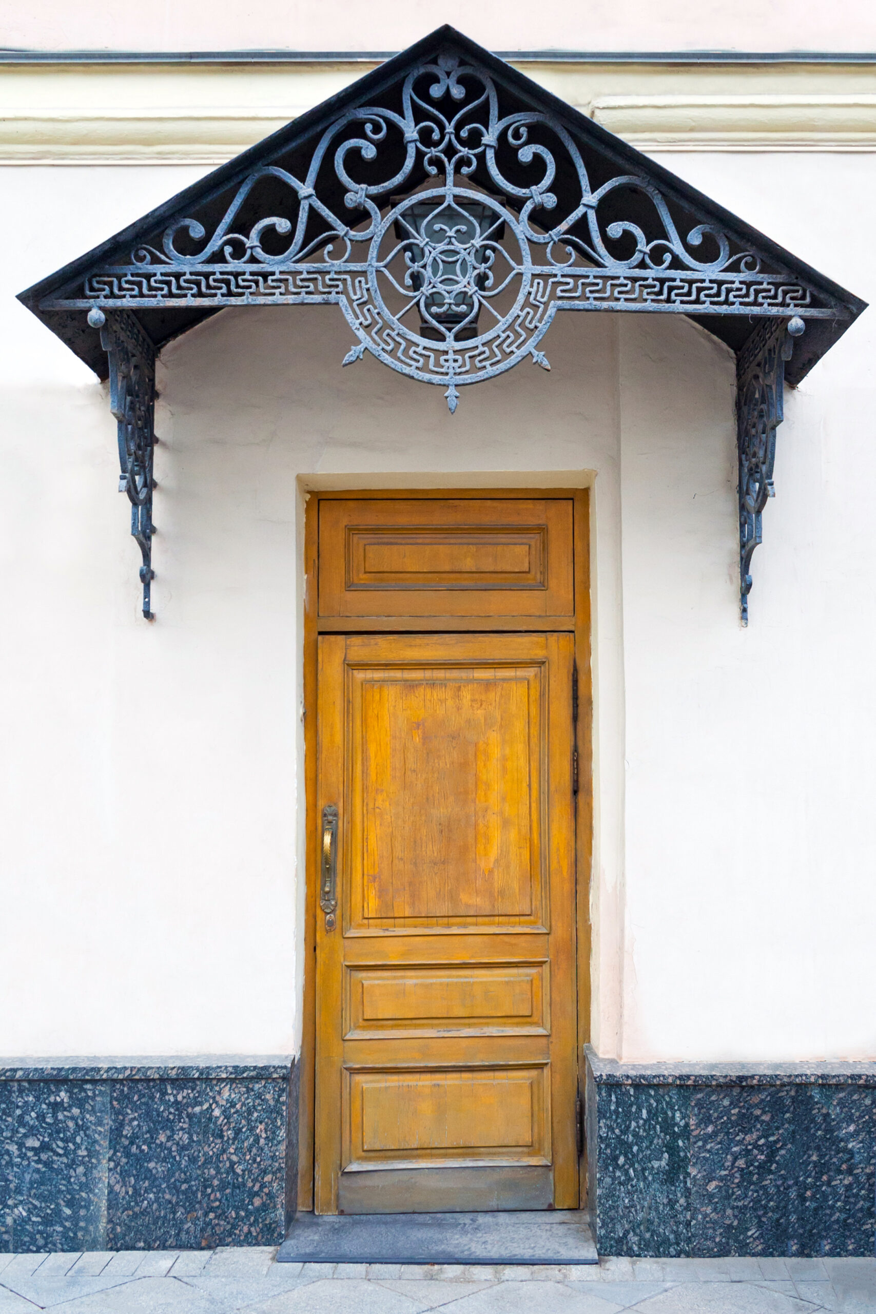 View on a porch with brown wooden door and forged decorative lattice on the pediment