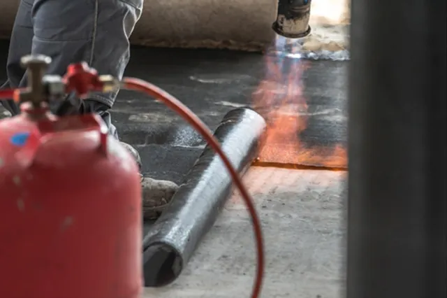 roofer next to propane gas torch, torching down a roofing membrane