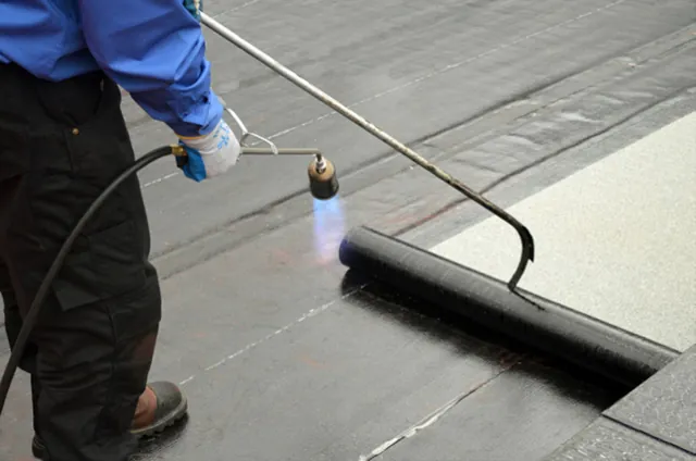 roofers torching down roofing membranes on a flat commercial roof