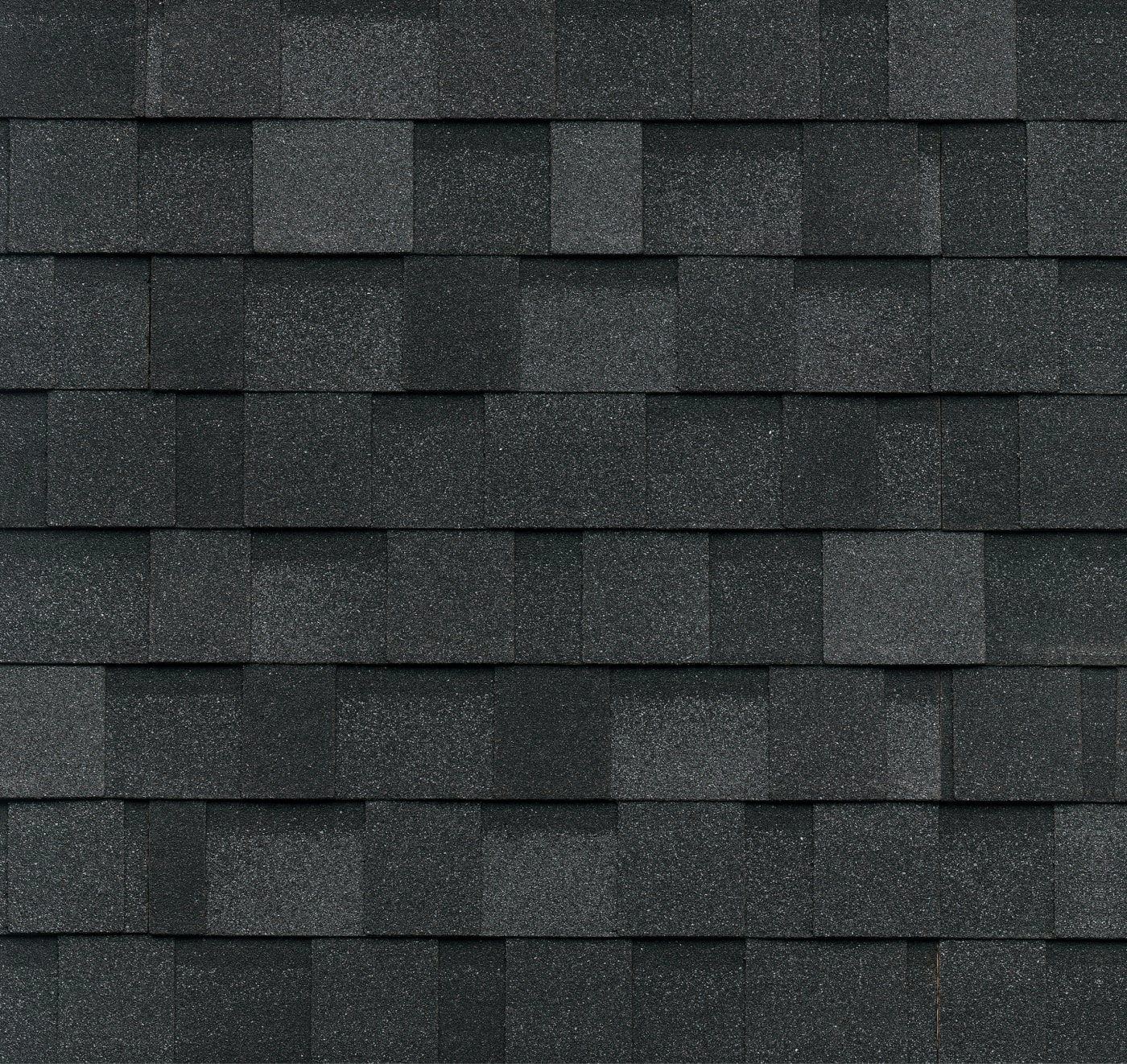 Close-up of black asphalt roof shingles arranged in an overlapping, dynasty-like pattern reminiscent of polished granite.