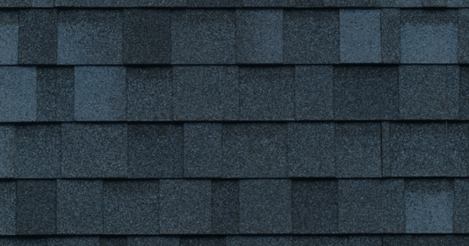 Close-up of a roof with overlapping dark gray asphalt shingles arranged in a uniform pattern.