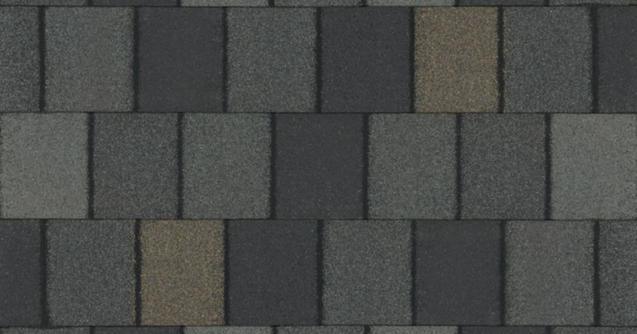 Close-up of a textured gray and black roof shingle pattern with vertical and horizontal rectangles.