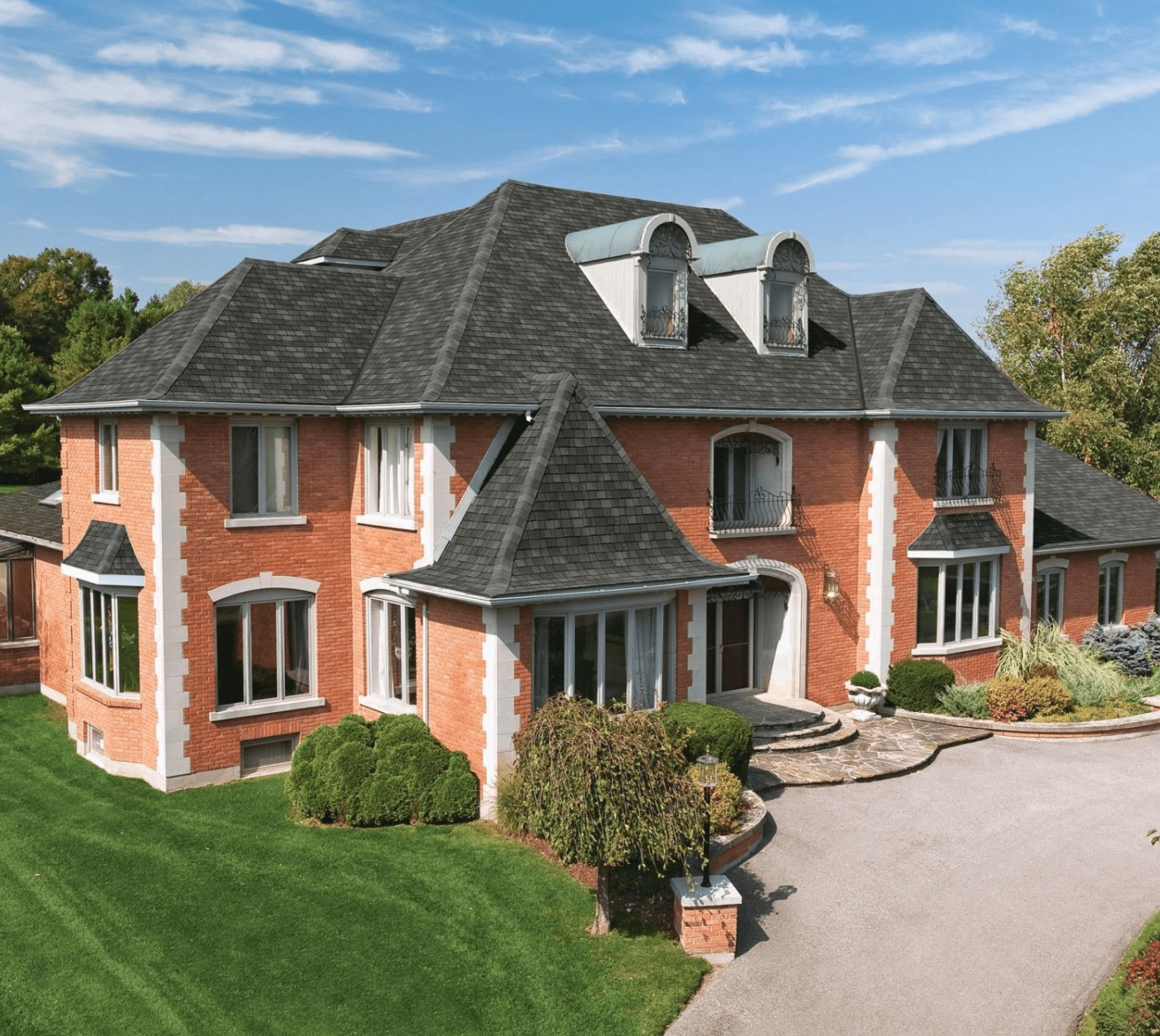 Large Nordic-inspired two-story brick house with dark roof, multiple windows, and landscaped front yard. A curved driveway leads to the entrance under a partly cloudy sky, embodying Scandinavian charm.