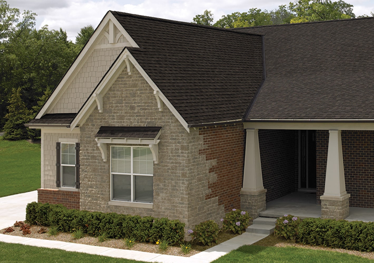 Front view of a modern house in Cambridge with a brick facade, dark shingle roof, and a small porch. Shrubs and a concrete path create an inviting entrance.