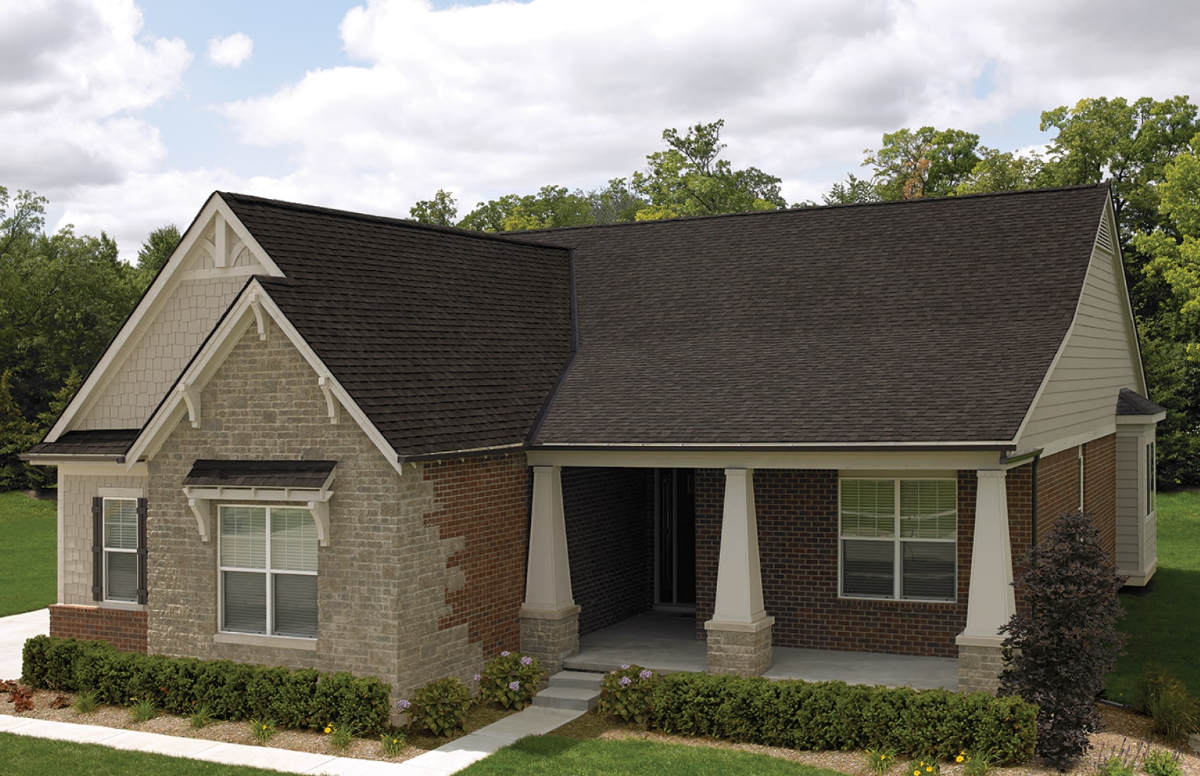 Front view of a modern house in Cambridge with a brick facade, dark shingle roof, and a small porch. Shrubs and a concrete path create an inviting entrance.