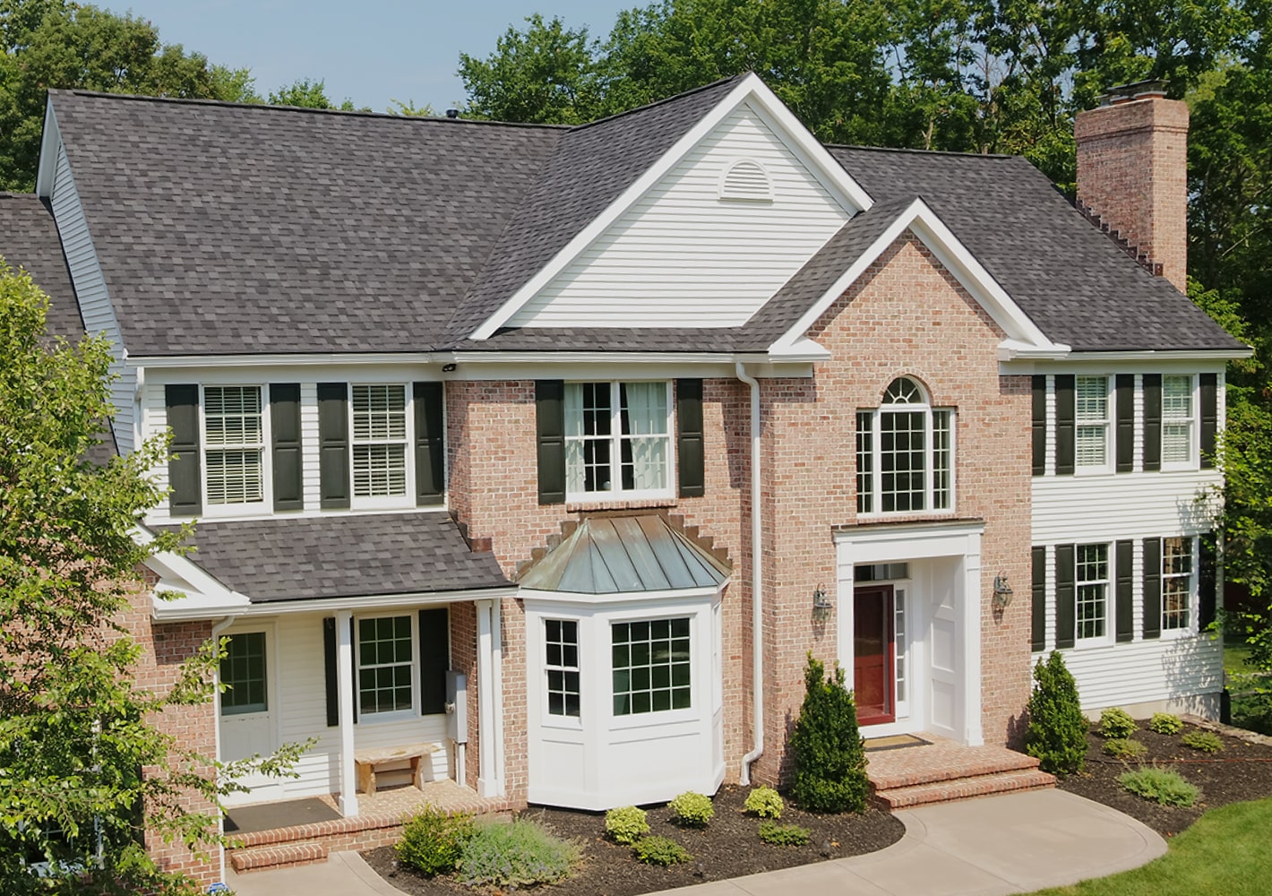 This two-story brick house showcases a touch of dynasty with its elegant white siding, black shutters, and shingled roof. The striking red front door and bay window invite you into a beautifully landscaped front yard.