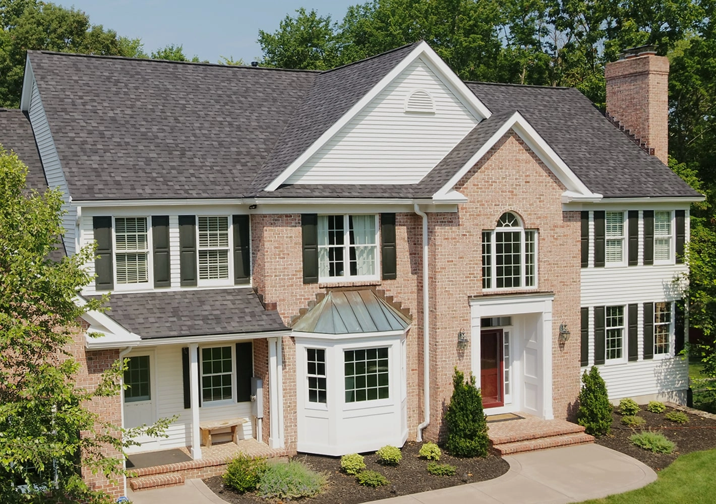 This two-story brick house showcases a touch of dynasty with its elegant white siding, black shutters, and shingled roof. The striking red front door and bay window invite you into a beautifully landscaped front yard.