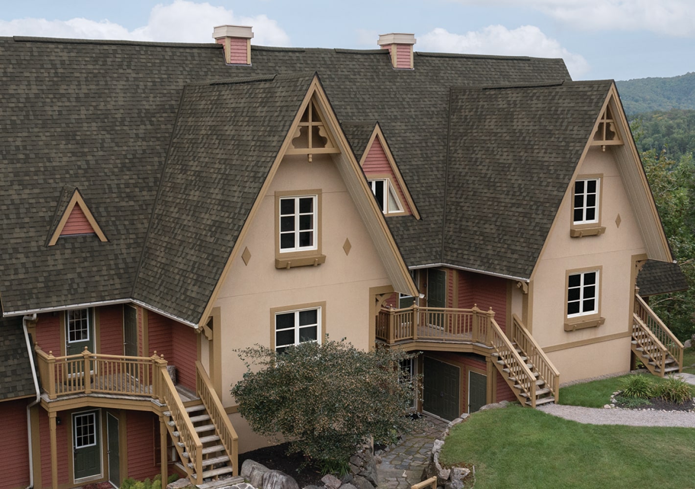 A Nordic™ chalet-style building with steep gabled roofs, wood accents, and exterior staircases is beautifully surrounded by lush greenery.