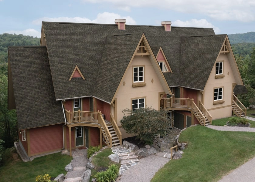 A Nordic-inspired two-story house with steep, dark roofs, beige walls, and multiple wooden staircases sits gracefully in a green, hilly landscape.