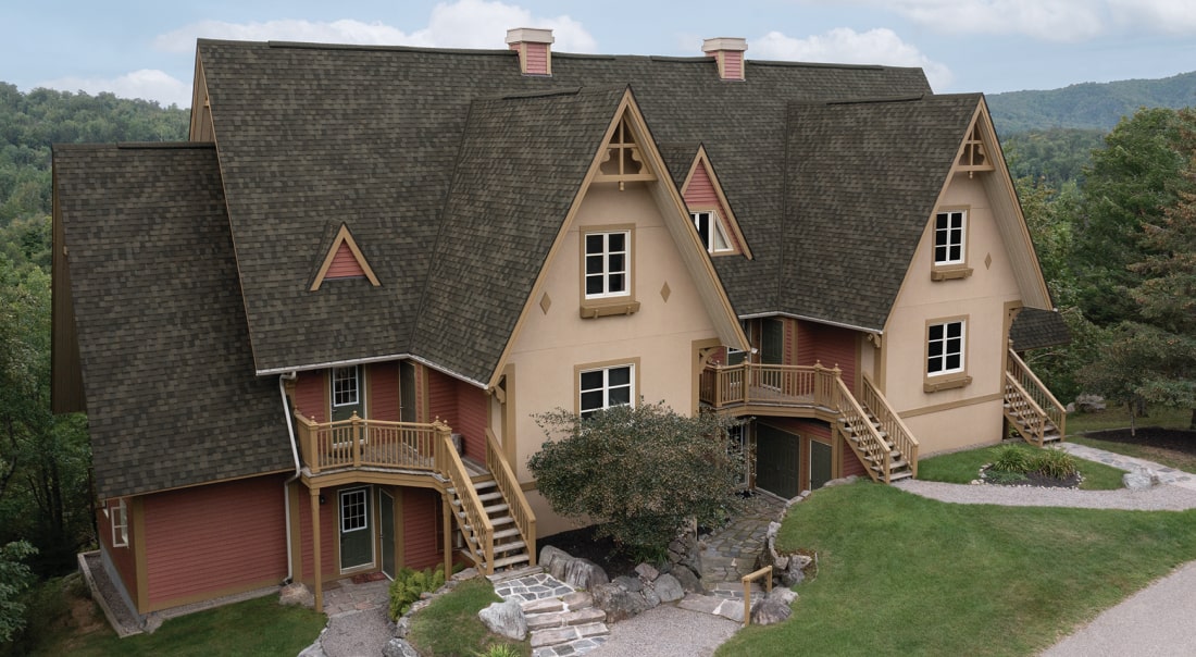 A Nordic™ chalet-style building with steep gabled roofs, wood accents, and exterior staircases is beautifully surrounded by lush greenery.