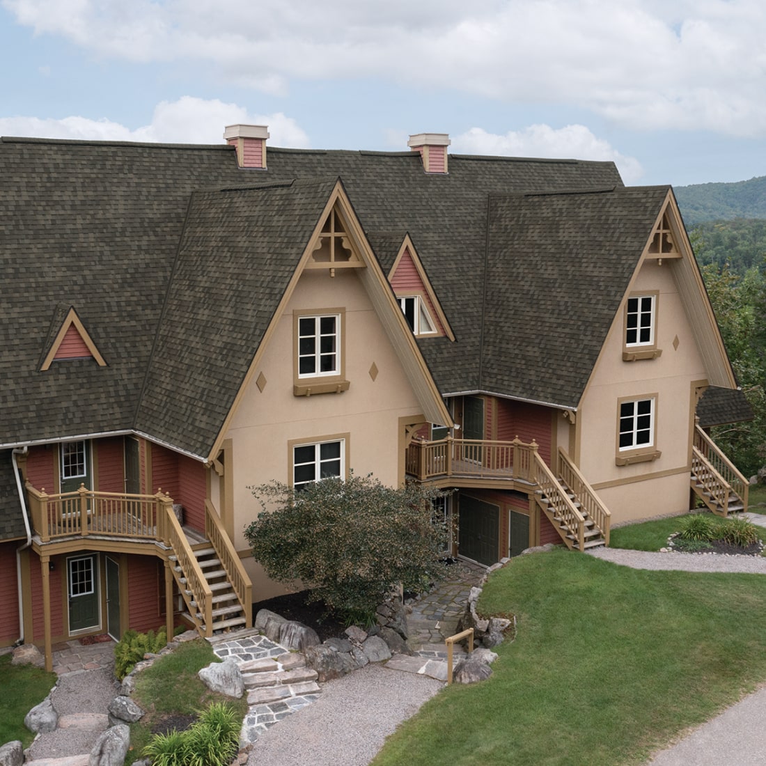 A Nordic™ chalet-style building with steep gabled roofs, wood accents, and exterior staircases is beautifully surrounded by lush greenery.