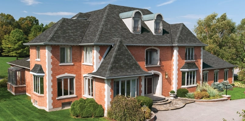 Large Nordic-inspired two-story brick house with dark roof, multiple windows, and landscaped front yard. A curved driveway leads to the entrance under a partly cloudy sky, embodying Scandinavian charm.