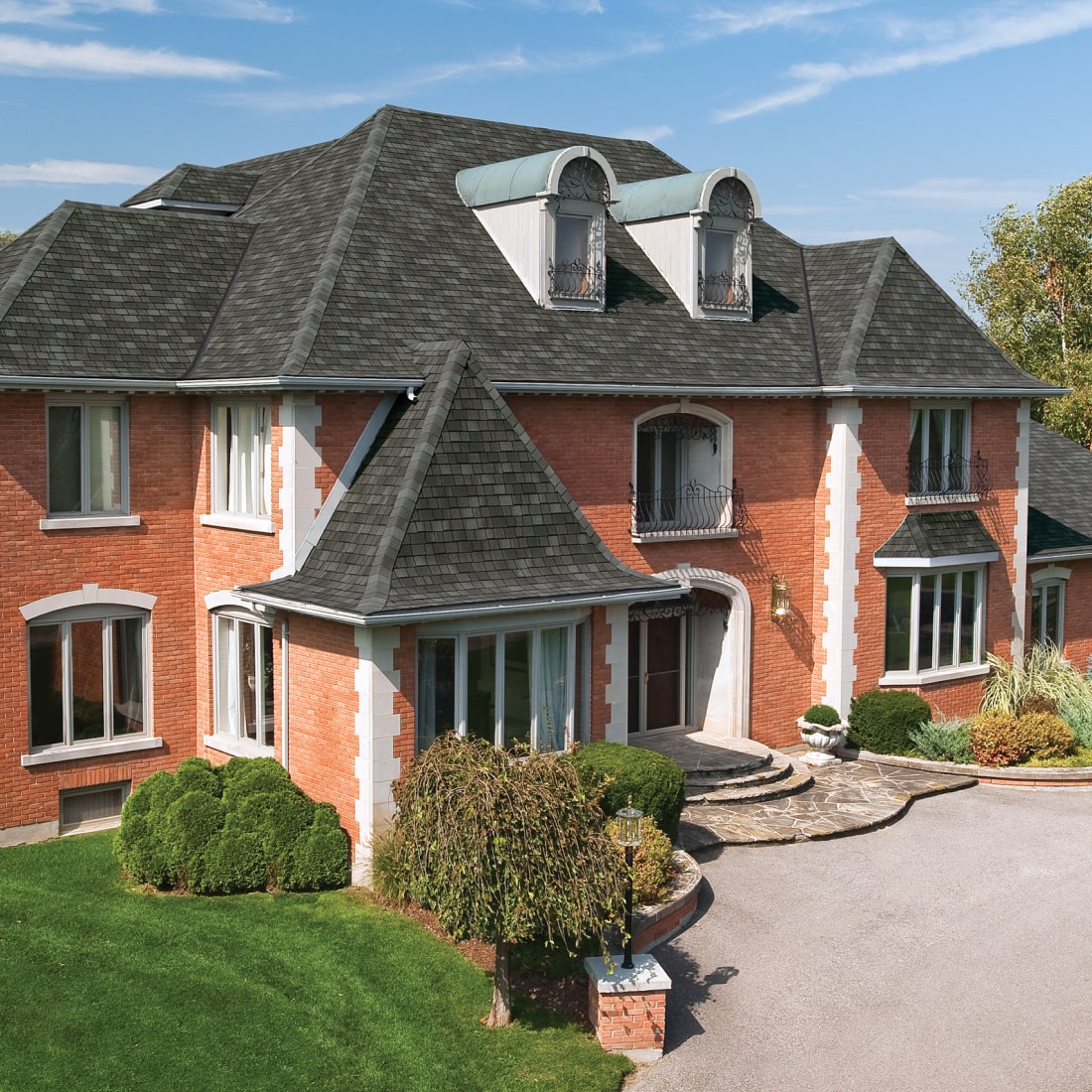 Large Nordic-inspired two-story brick house with dark roof, multiple windows, and landscaped front yard. A curved driveway leads to the entrance under a partly cloudy sky, embodying Scandinavian charm.