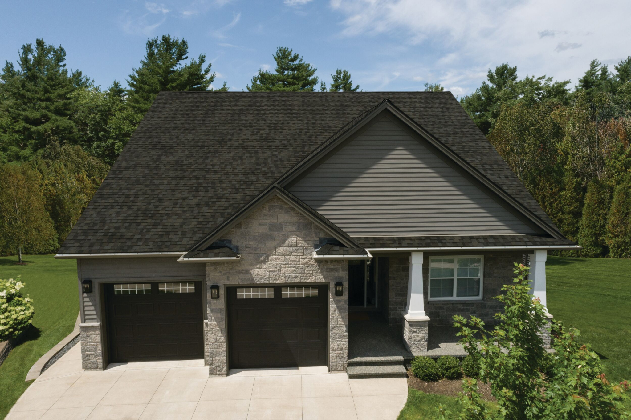 A Nordic-inspired suburban house with a dark roof and two garage doors, surrounded by lush greenery and trees, sits under a partly cloudy sky.