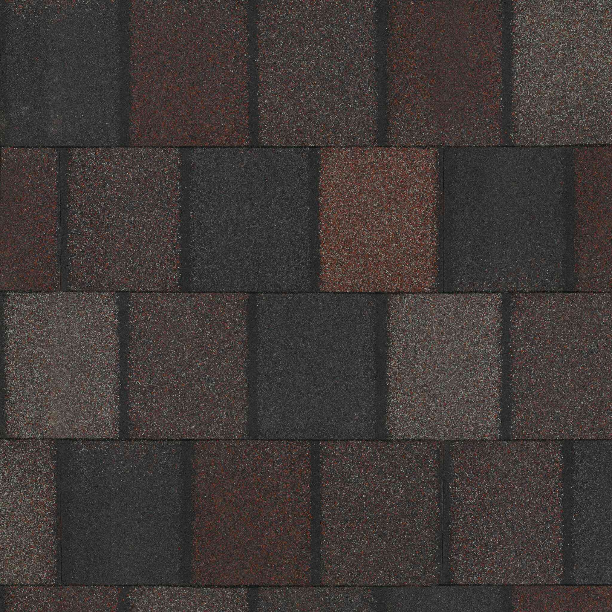 Asphalt roof shingles in shades of dark gray and brown, reminiscent of Royal Granite, are arranged in a repetitive pattern.