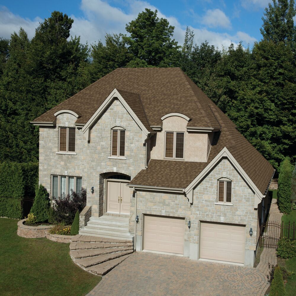 Front view of a modern house in Cambridge with a brick facade, dark shingle roof, and a small porch. Shrubs and a concrete path create an inviting entrance.