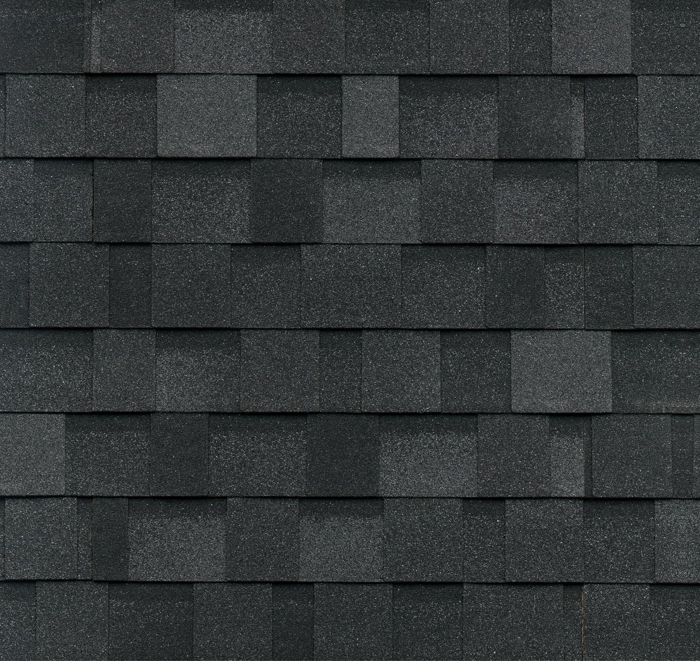 Close-up of a textured green asphalt shingle roof pattern with evenly arranged rectangular shingles, subtly accented by hints of granite tones.