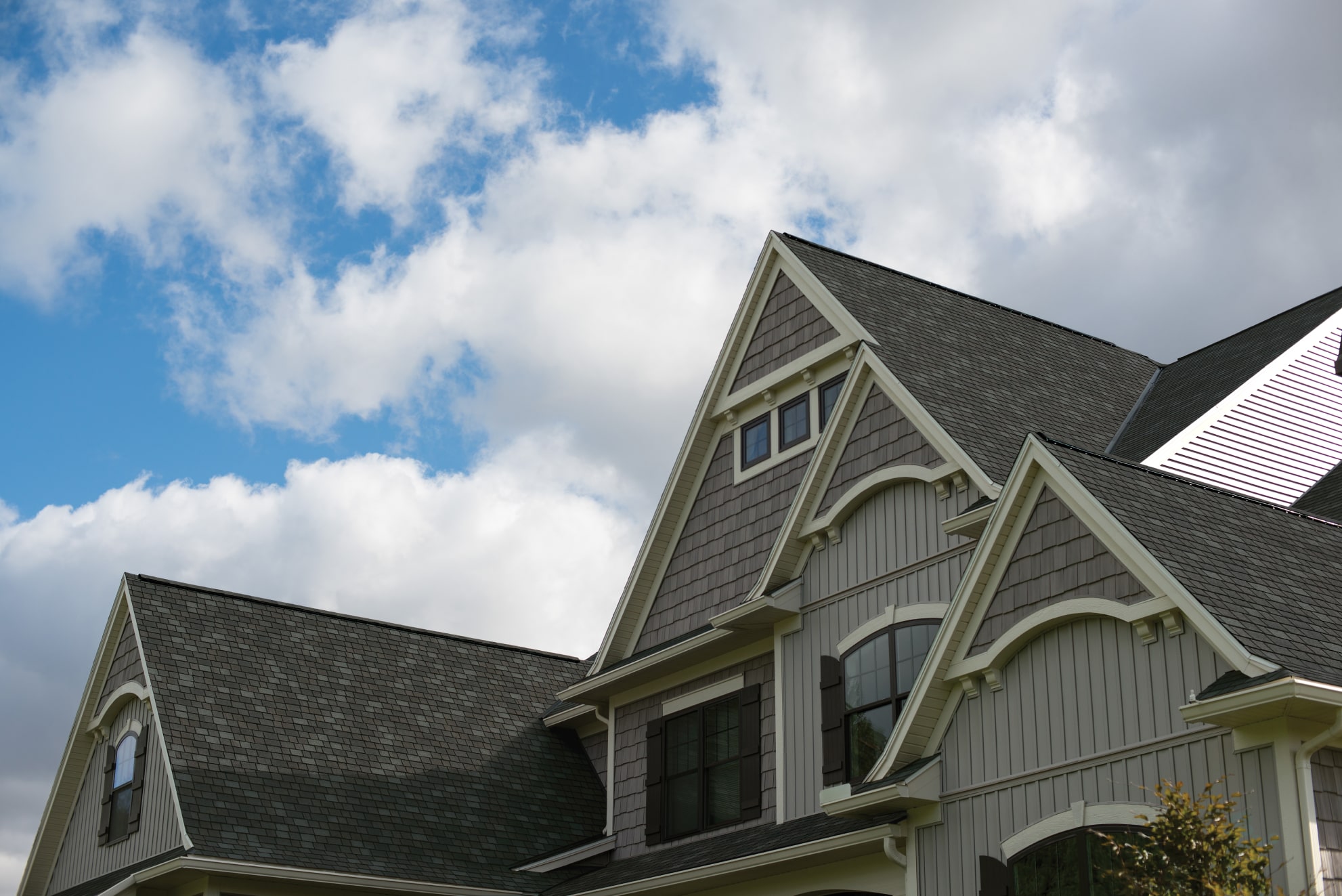 The gabled roof of a large house, resembling the elegance of a Royal Estate, stands prominently under the partly cloudy sky.