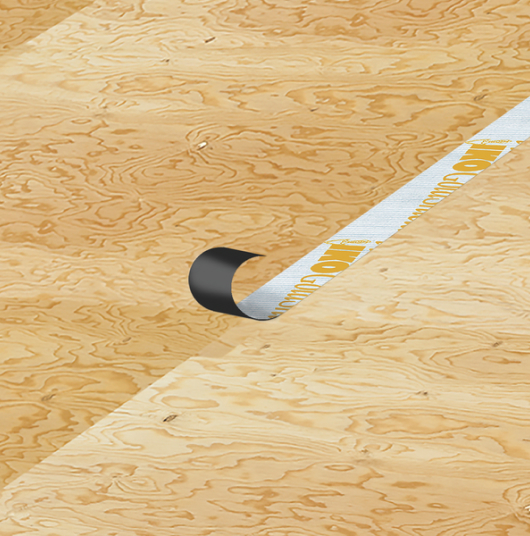 A roll of Gold Seam™ black and white tape partially unrolled on plywood flooring.