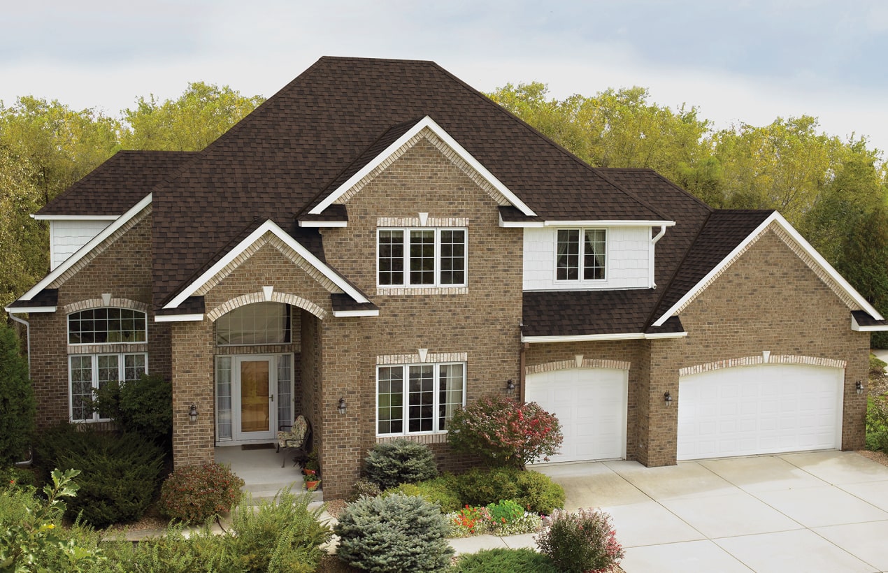 Front view of a modern house in Cambridge with a brick facade, dark shingle roof, and a small porch. Shrubs and a concrete path create an inviting entrance.