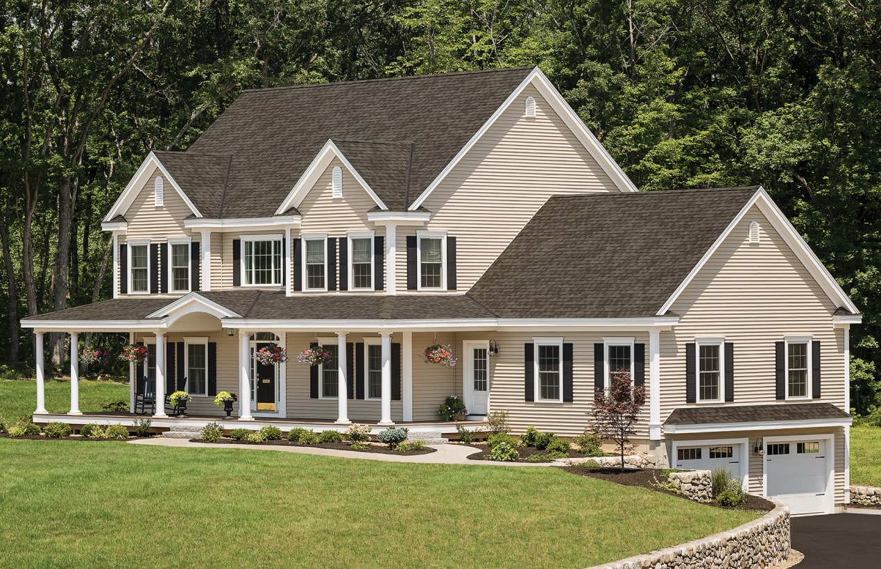 Front view of a modern house in Cambridge with a brick facade, dark shingle roof, and a small porch. Shrubs and a concrete path create an inviting entrance.