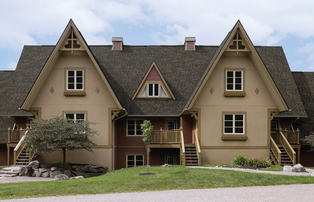 A Nordic™ chalet-style building with steep gabled roofs, wood accents, and exterior staircases is beautifully surrounded by lush greenery.