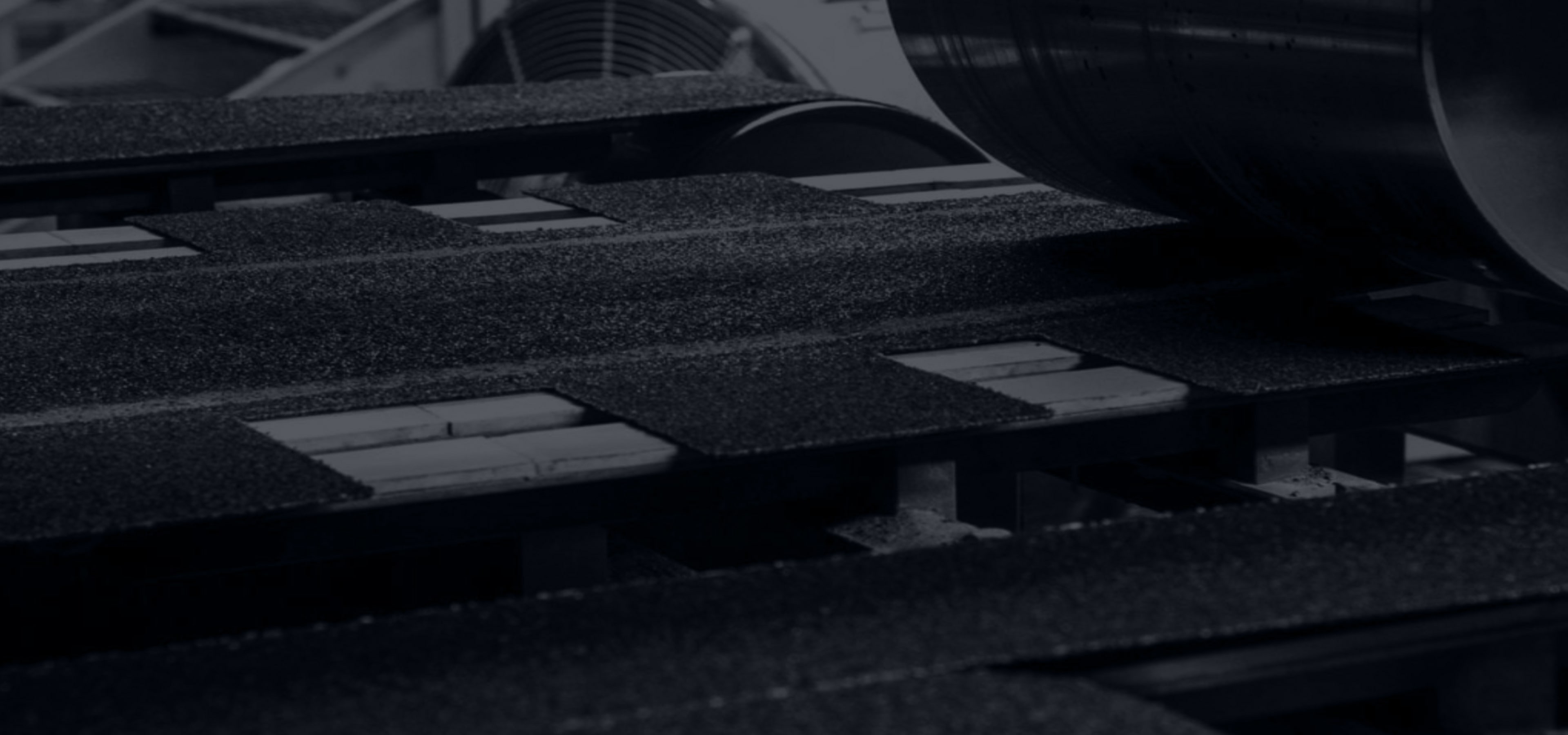 Dark industrial machinery in an IKO manufacturing facility meticulously processes asphalt shingles, offering homeowners durable roofing solutions.