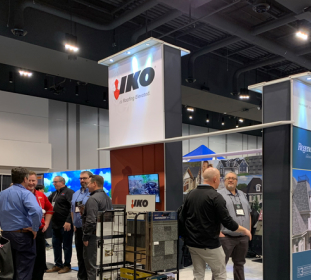 People networking at an IKO booth in a convention center, with displays of roofing materials and company signage visible.