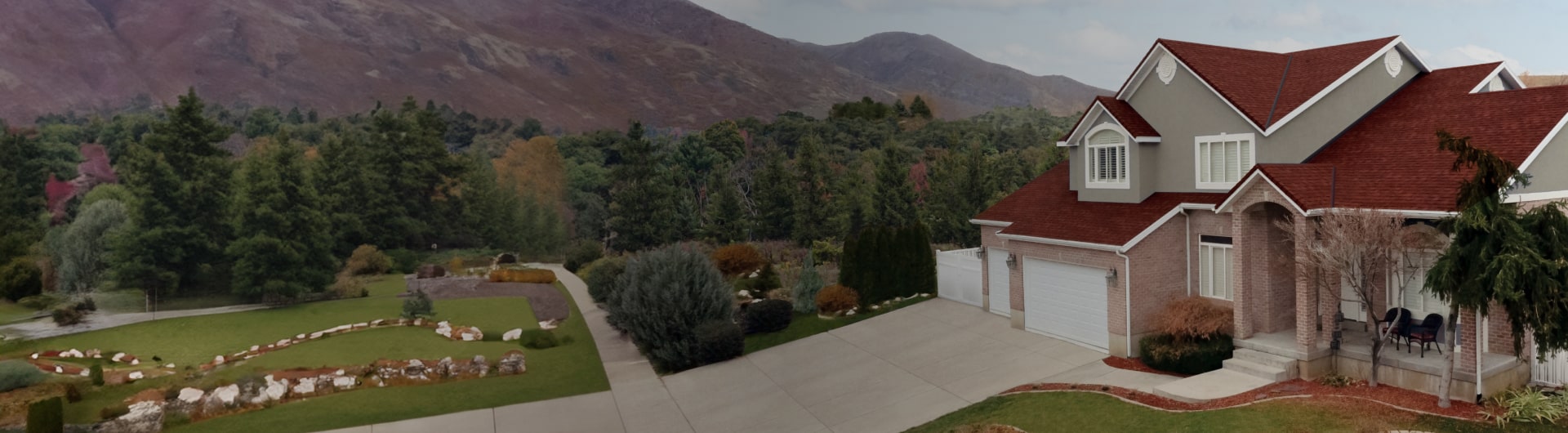 House with a red roof and gray exterior, exuding inspiration in every design aspect. Surrounded by a well-maintained yard, it features a driveway and is set against a mountain backdrop with lush greenery.