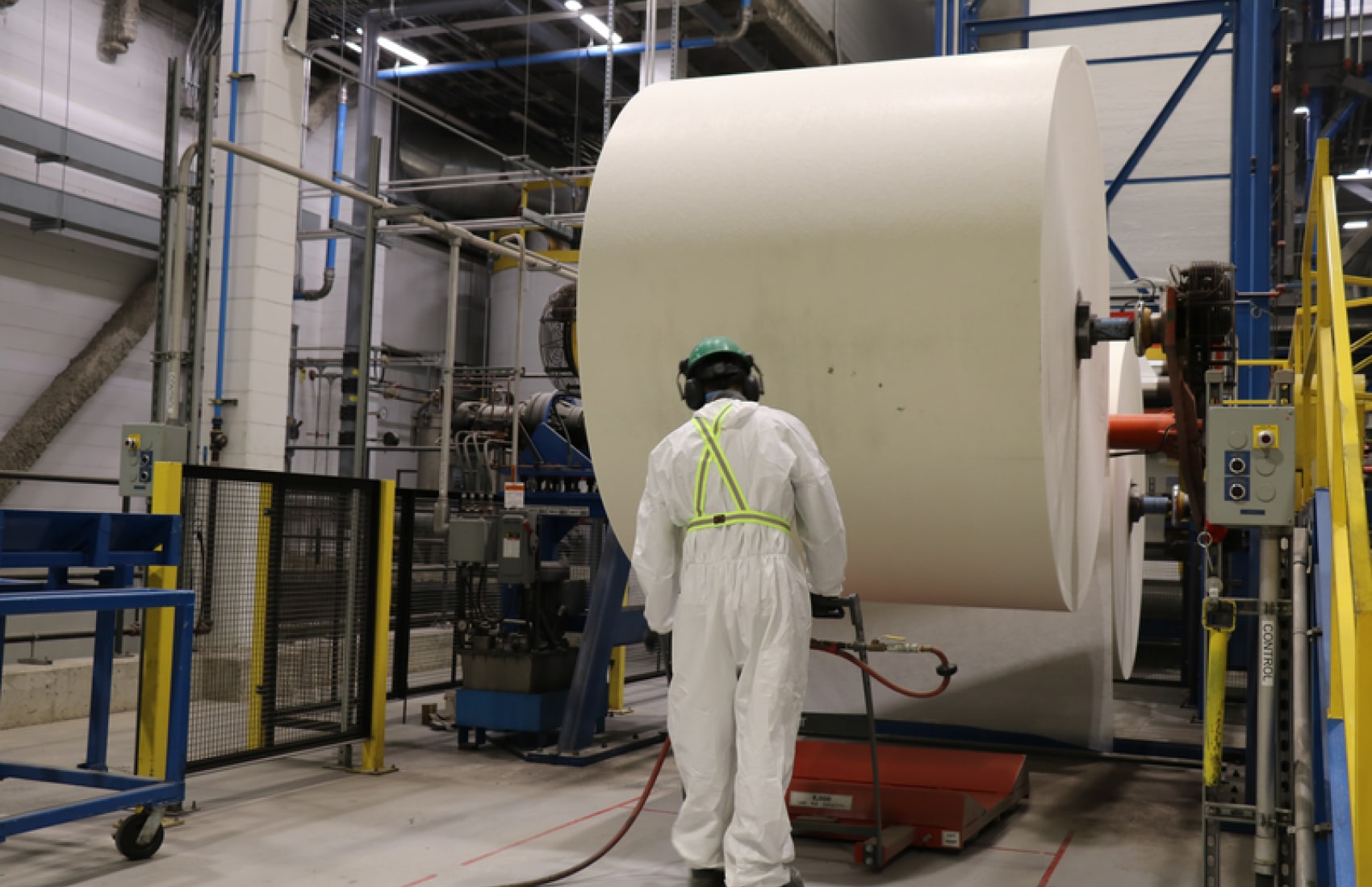 A worker in protective gear manages machinery near a large paper roll in an industrial setting, showcasing the IKO Difference.