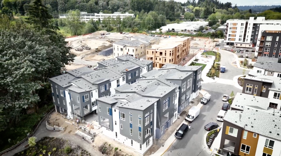 Aerial view of a multifamily residential construction site featuring completed townhouses and ongoing building work, surrounded by greenery and modern buildings, with IKO x Chinook materials enhancing the development.