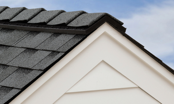 A section of a house roof with UltraHP dark shingles and white siding, viewed from an angle against a light blue sky background, creates a striking contrast.