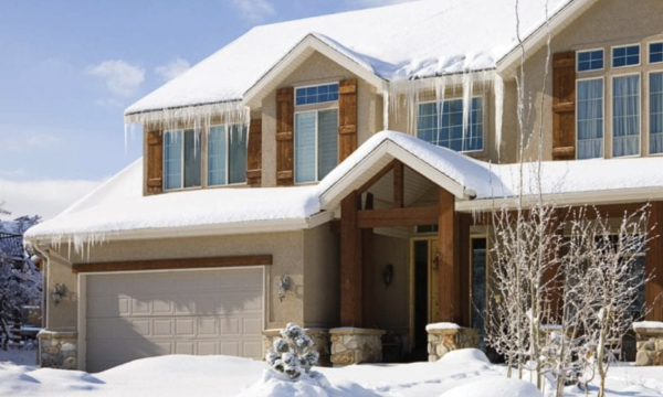 A house with a gabled roof, grey shingles, stone facade, and green window shutters offers robust storm shield features. One section of the roof is currently under construction, ensuring enhanced weather protection.