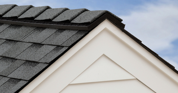 A section of a house roof with UltraHP dark shingles and white siding, viewed from an angle against a light blue sky background, creates a striking contrast.