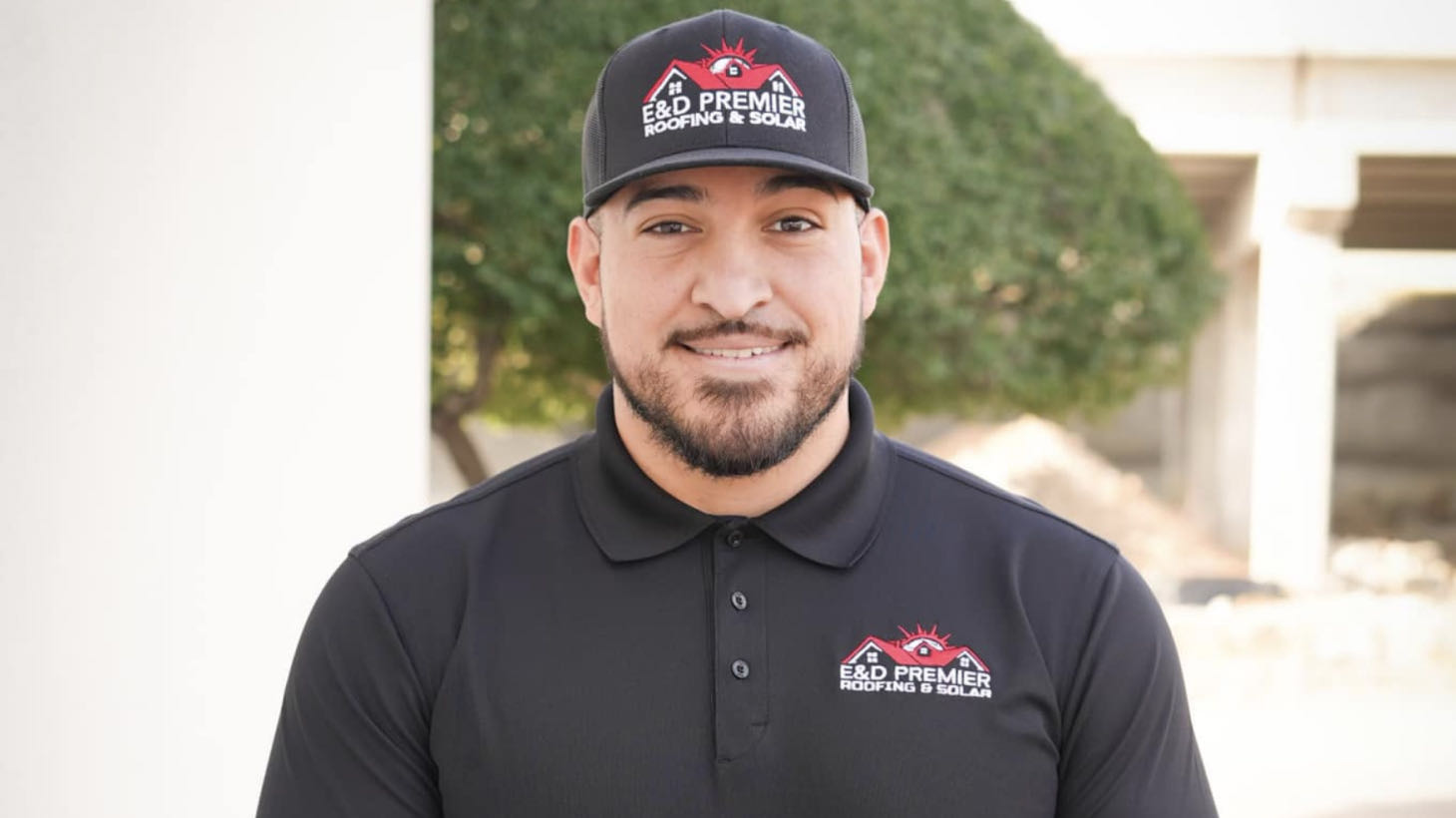 A man wearing a black polo shirt and cap featuring the ROOFPRO logo stands outside against a blurred backdrop, showcasing the benefits of expert roofing services.