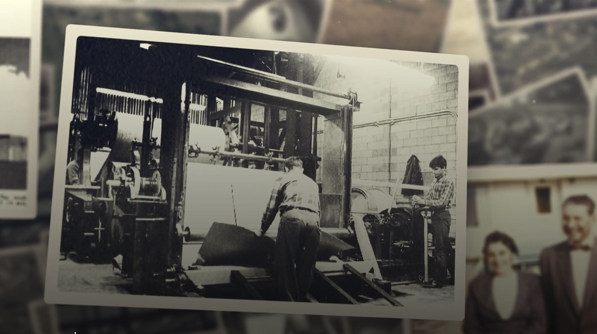 In this black-and-white photo, dedicated workers operate a large industrial machine in an IKO factory setting. Two men are intensely focused on handling materials, showcasing the difference that skilled craftsmanship brings to every operation.