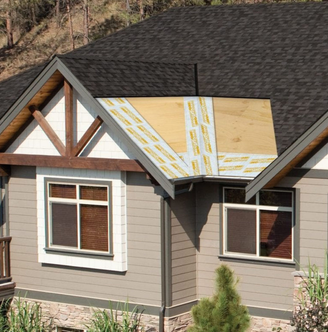 The house exterior features a shingled roof, partly shielded by exposed wooden boards and adhesive strips, with the durable protection of Gold Shield™, all nestled amidst lush trees and shrubs.