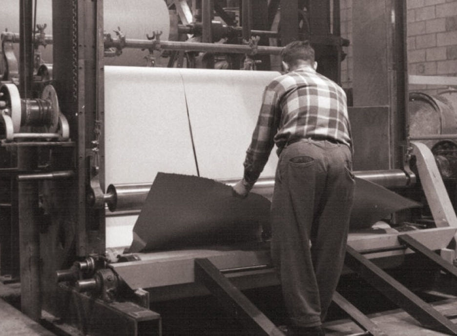 Worker operating a paper-cutting machine, adjusting paper sheet alignment with precision reminiscent of advanced technology.