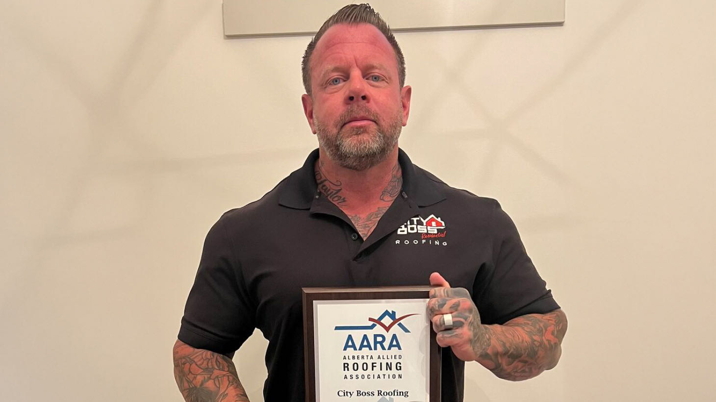 A person with tattoos holds a framed certificate from the Alberta Allied Roofing Association for City Boss Roofing, proudly showcasing the benefits of being recognized as a top ROOFPRO member.