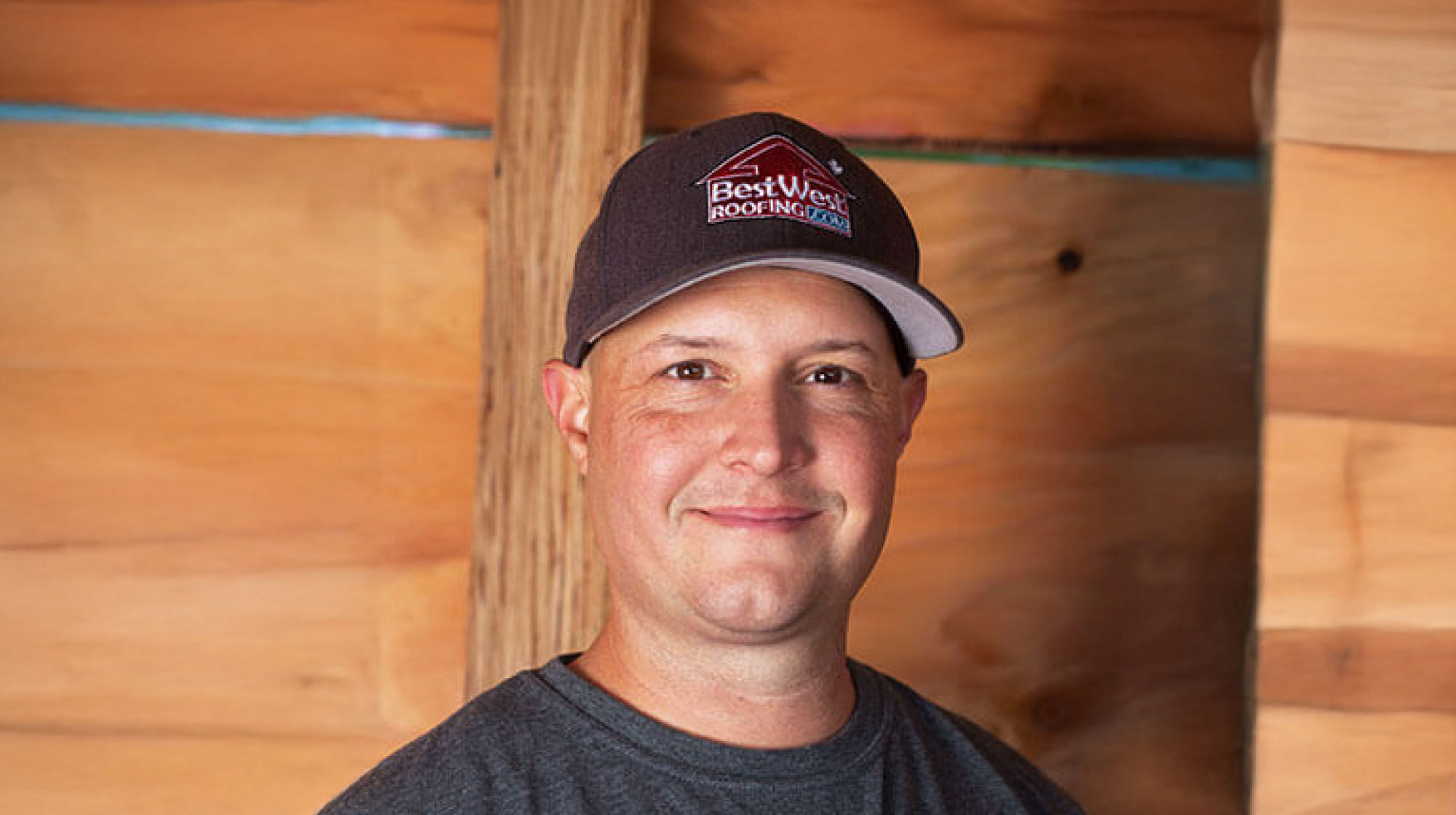 A person wearing a cap with an IKO logo stands in front of a wooden wall, smiling slightly at the camera, embodying the friendly professionalism that sets them apart.