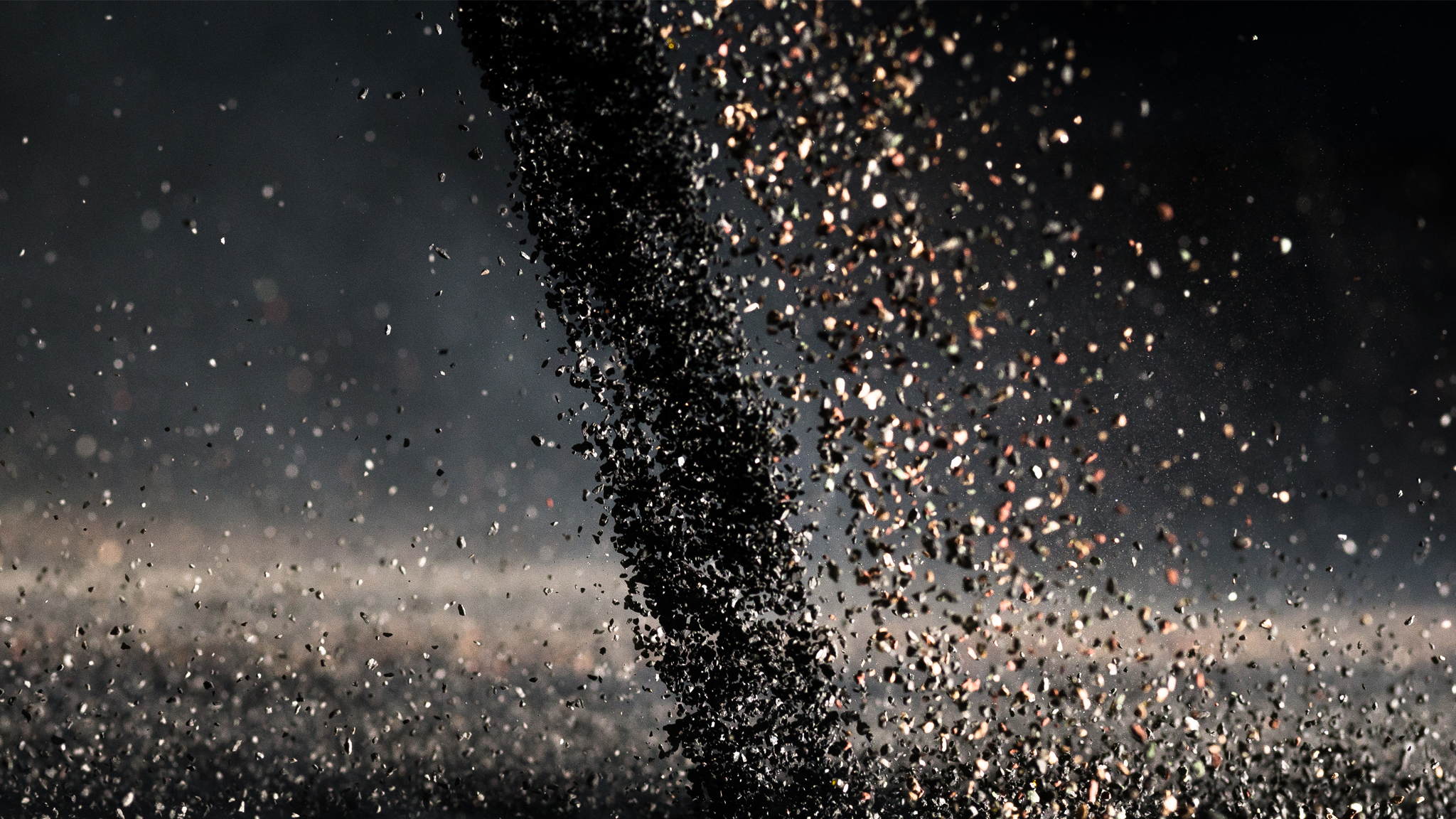 A swirling vortex of dark particles, possibly sand or debris from a granule facility, is captured mid-motion against a dark background, creating a dynamic and textured visual effect reminiscent of Missouri's stormy skies.