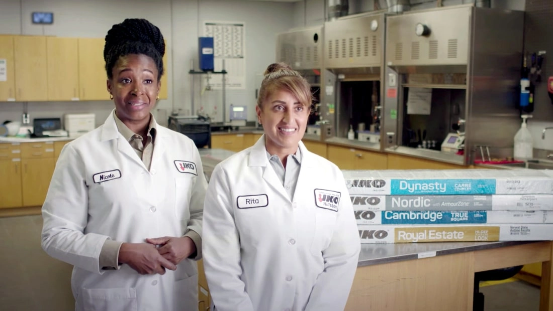 Two lab technicians in white coats stand amidst the bustling laboratory, surrounded by equipment and materials. One wears a name tag reading "Kim" and the other "Rita," both eagerly discussing the promising career opportunities their work could unlock.