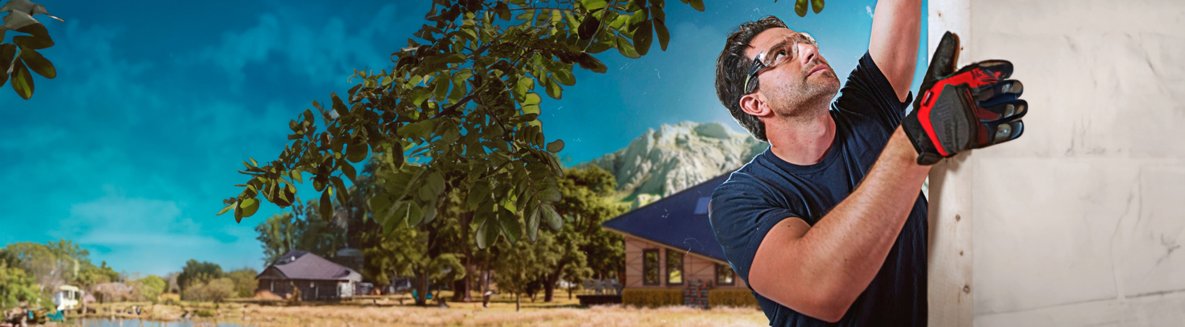 Man in safety glasses and gloves, reminiscent of a scene from a Scott McGillivray renovation show, works diligently on a structure. In the background, charming houses are nestled against the serene backdrop of towering mountains.