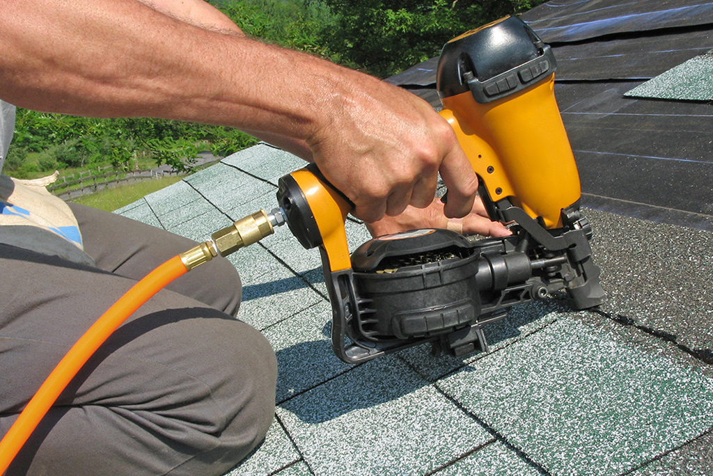 roofer using nail gun to install roof shingles